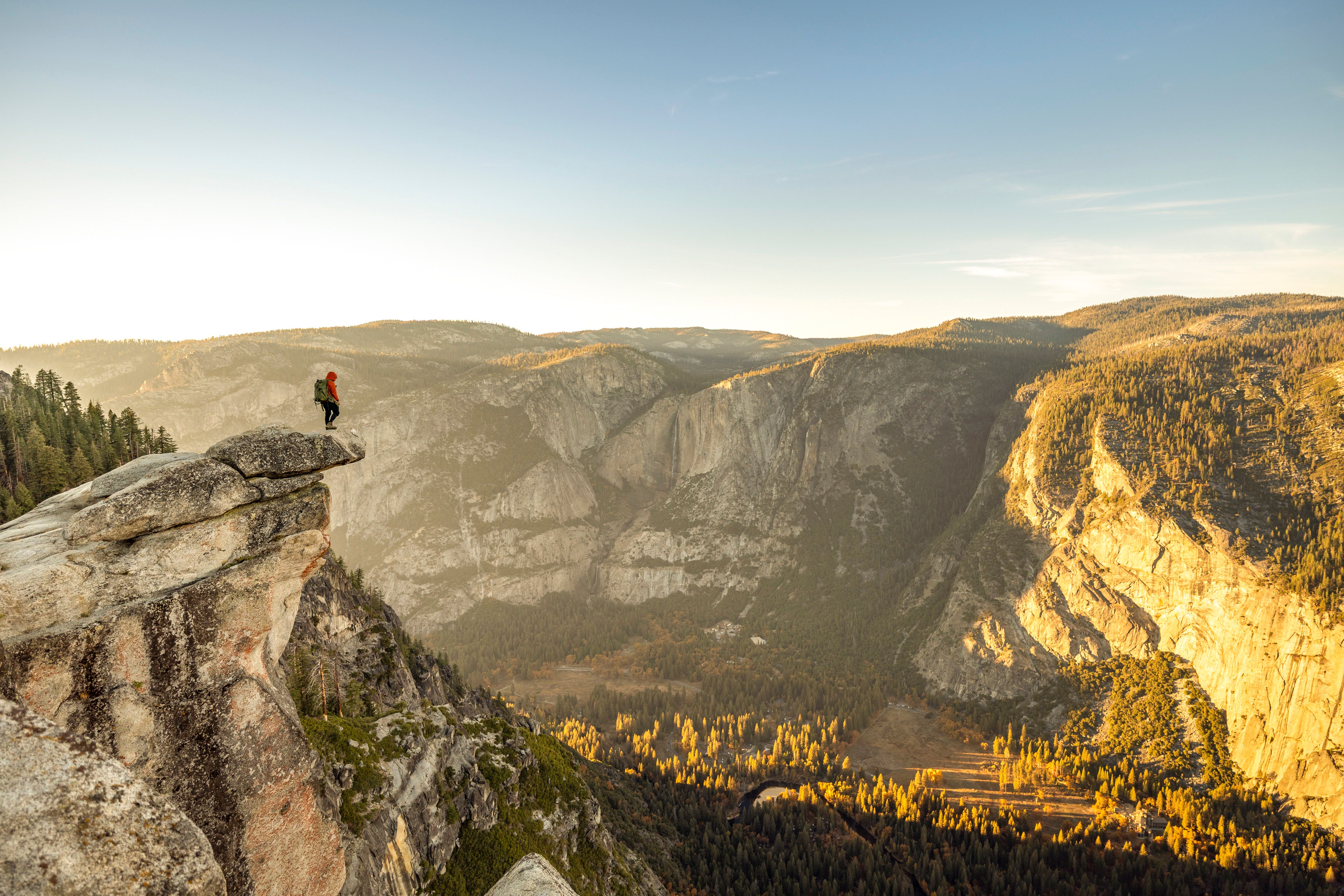 A hiker on a granite overlook above a sunlit valley of golden autumn trees